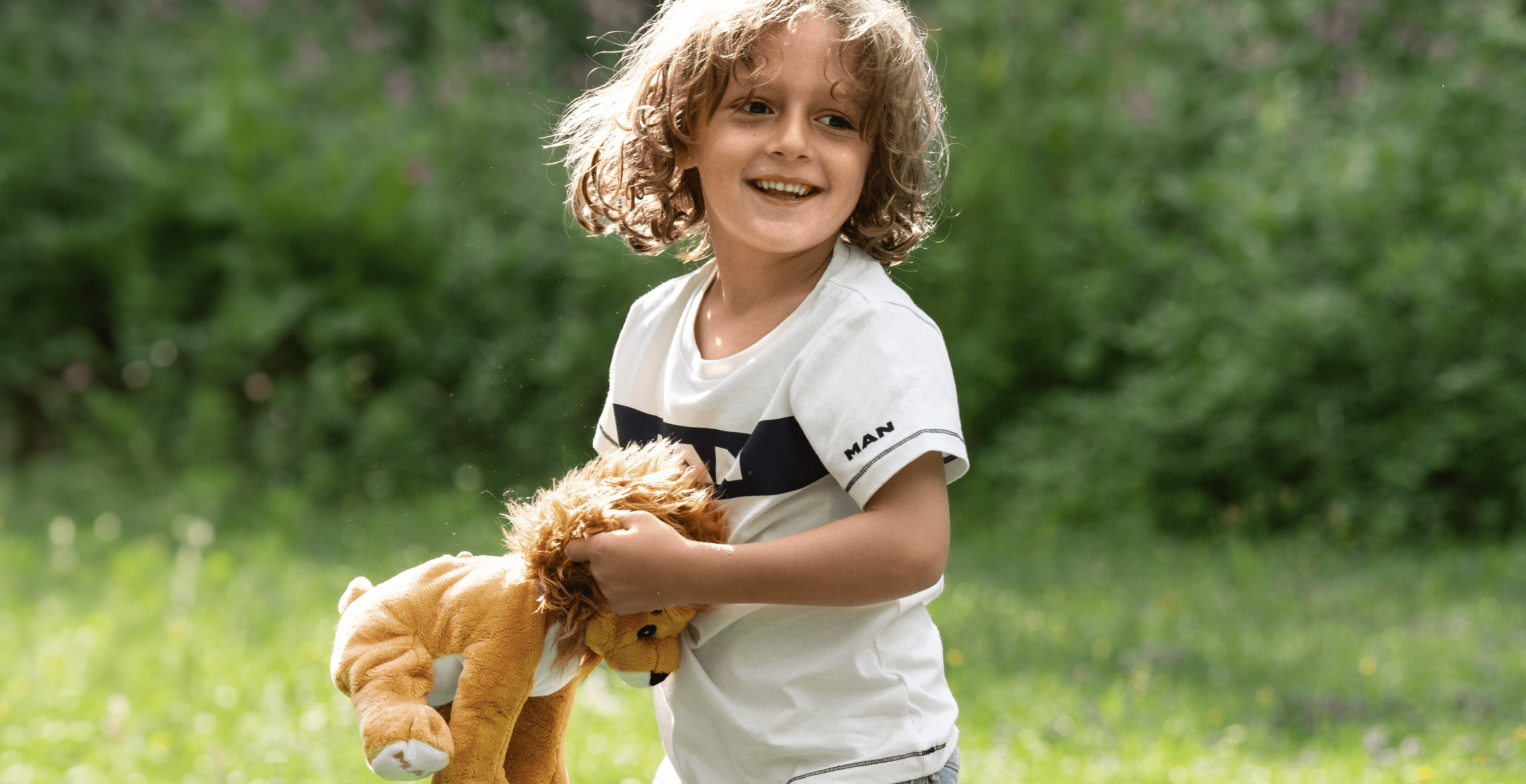 Lächelndes Kind in einem MAN-T-Shirt hält ein Löwen-Plüschtier, perfekt für aktive Kinder, die bequeme und stylische Kleidung lieben.